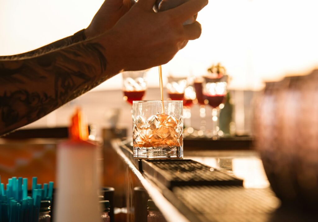 pexels-photo-8817296-8817296 A close-up of a bartender making cocktails at a bar during sunset, showcasing expert mixology skills.